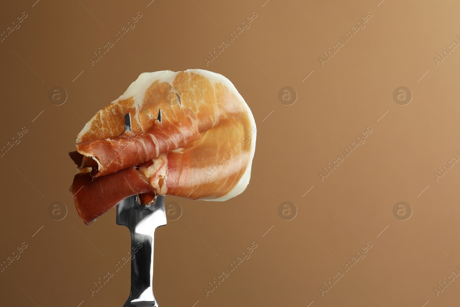 Photo of Fork with slice of tasty jamon on brown background, closeup. Space for text