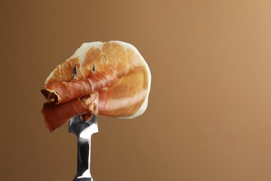 Photo of Fork with slice of tasty jamon on brown background, closeup. Space for text