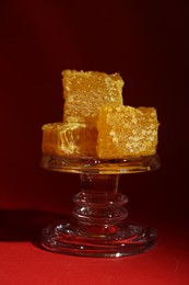 Photo of Natural honeycombs on glass stand against burgundy background