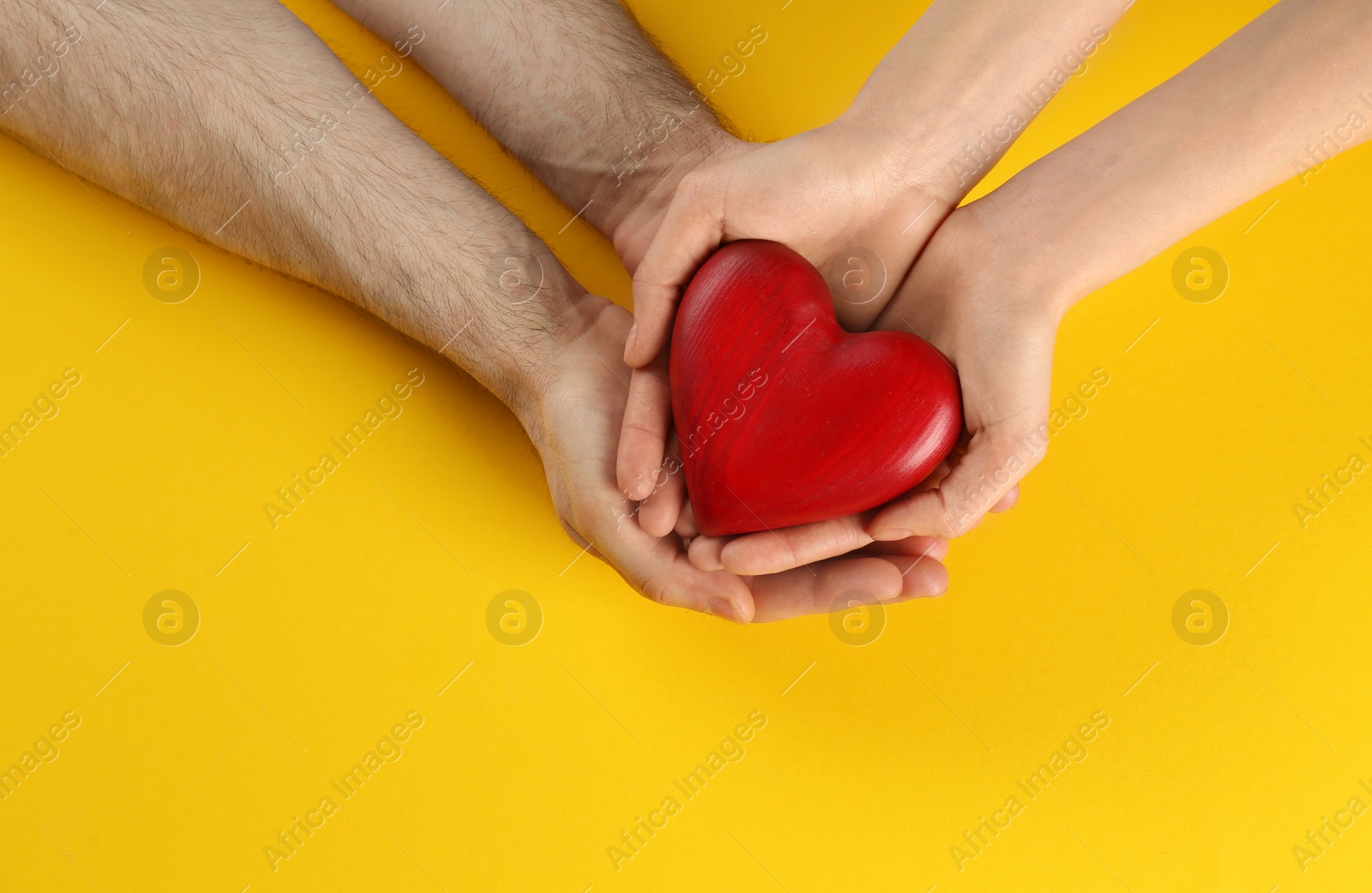 Photo of Couple holding decorative heart on color background, top view