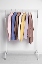 Warm sweaters hanging on rack near white wall