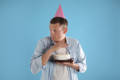 Greedy man with party hat hiding birthday cake on turquoise background
