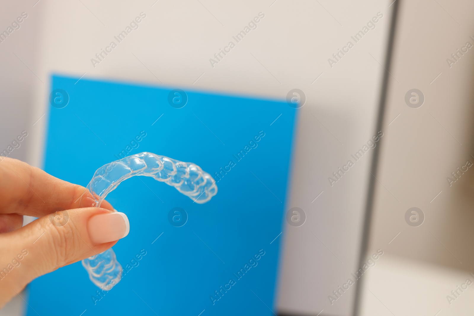 Photo of Woman with transparent dental aligner on blurred background, closeup. Space for text