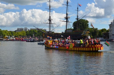 Photo of AMSTERDAM, NETHERLANDS - AUGUST 06, 2022: Boats with people holding LGBT pride flags at parade on river