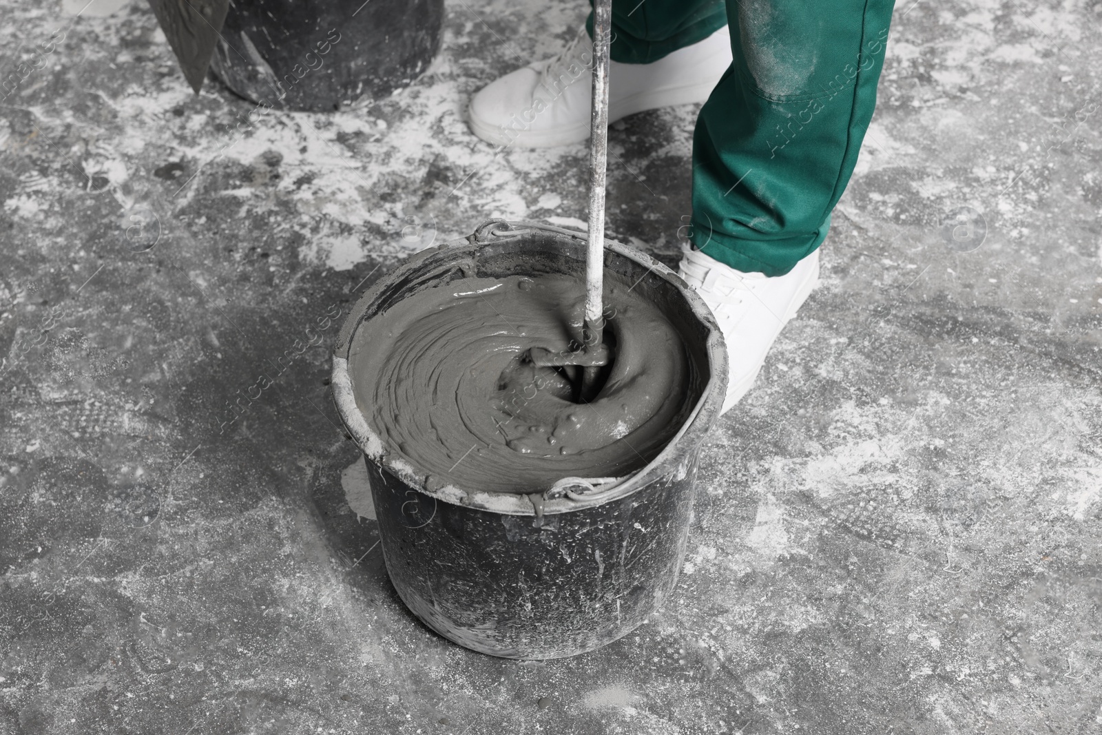 Photo of Worker mixing concrete in bucket indoors, closeup