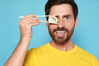 Photo of Happy man hiding his eye with tasty sushi roll on light blue background