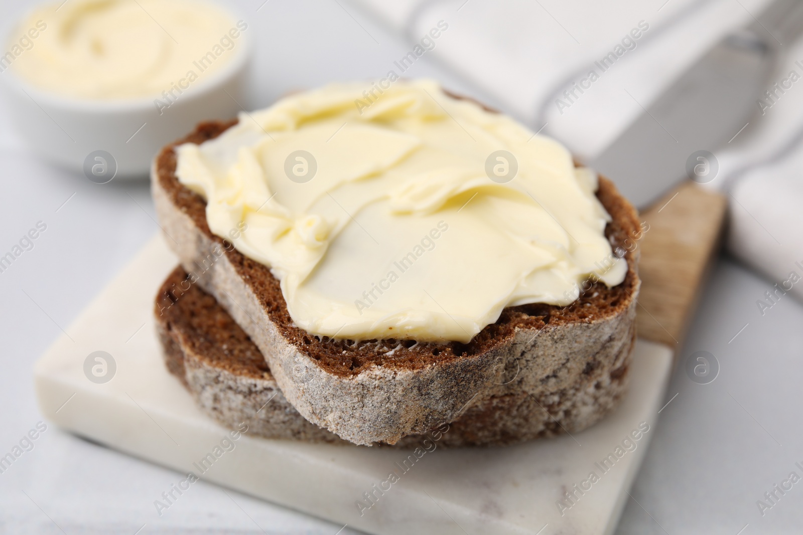 Photo of Slices of tasty bread with butter on white table, closeup