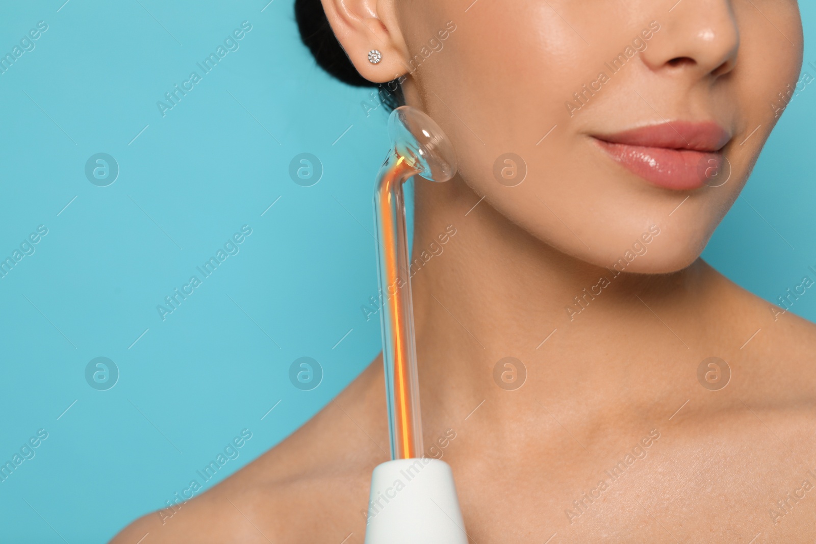 Photo of Woman using high frequency darsonval device on light blue background, closeup. Space for text