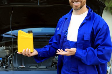 Worker showing yellow container of motor oil near car outdoors, closeup