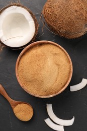 Spoon with coconut sugar, bowl and fruits on dark textured table, flat lay