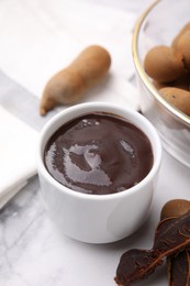 Photo of Bowl of tamarind sauce and fresh pods on white marble table