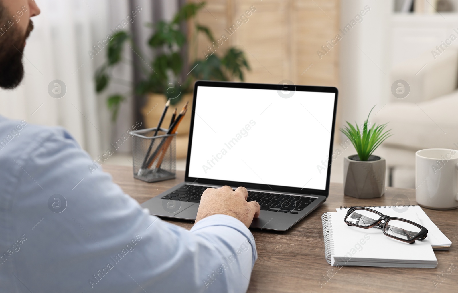 Photo of E-learning. Young man using laptop at wooden table indoors, closeup