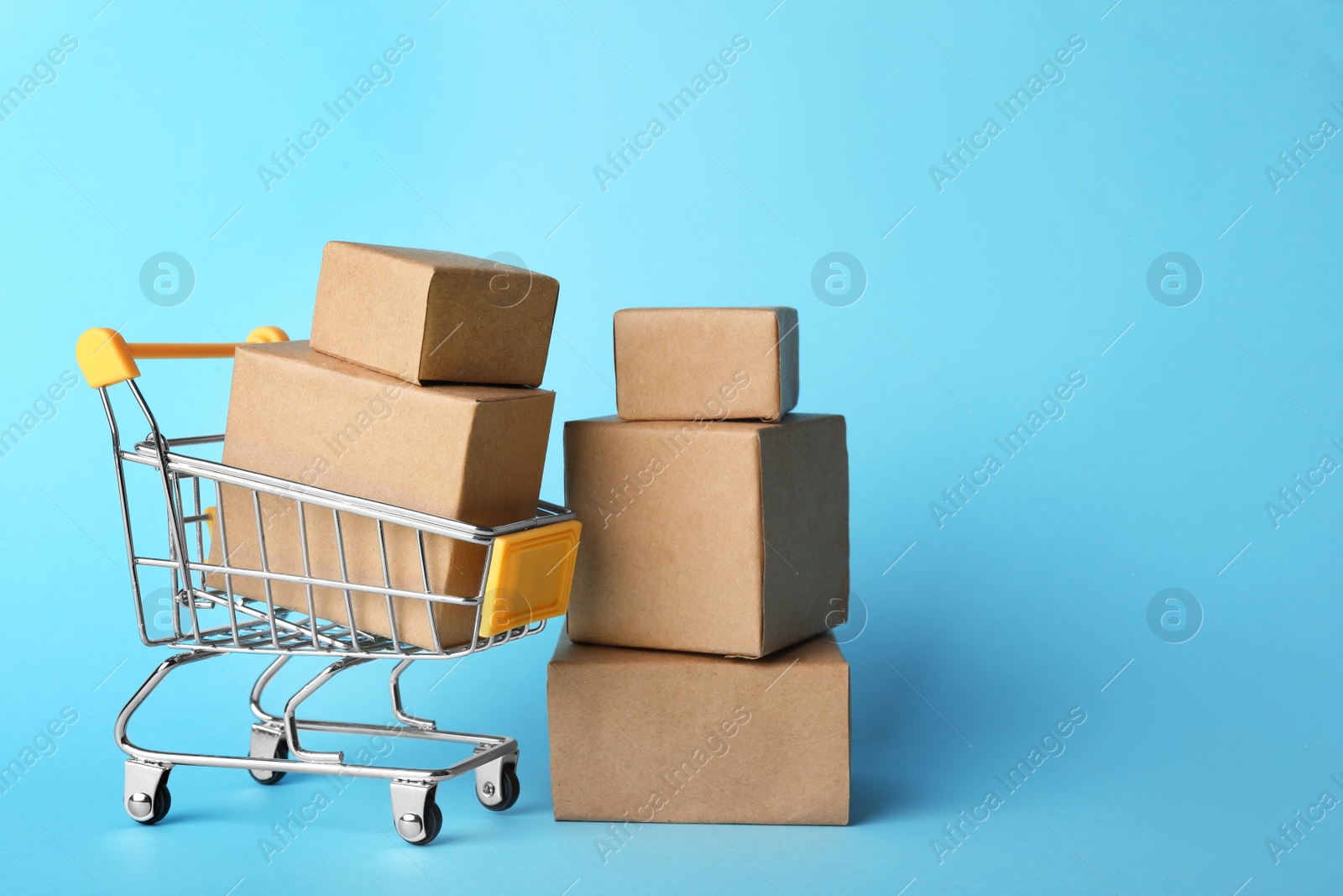 Photo of Shopping cart and boxes on light blue background, space for text. Logistics and wholesale concept