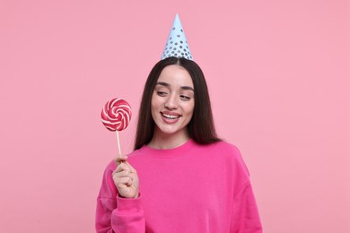 Woman in party hat holding lollipop on pink background