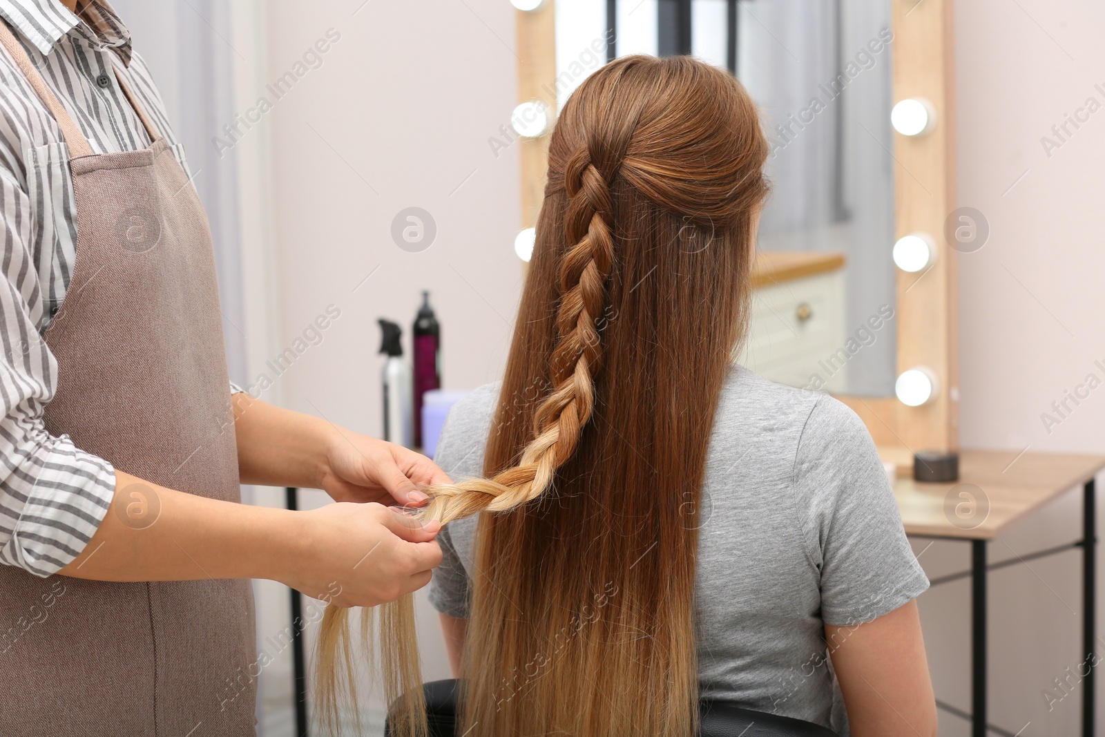 Photo of Professional coiffeuse braiding client's hair in salon