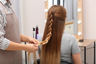 Professional coiffeuse braiding client's hair in salon