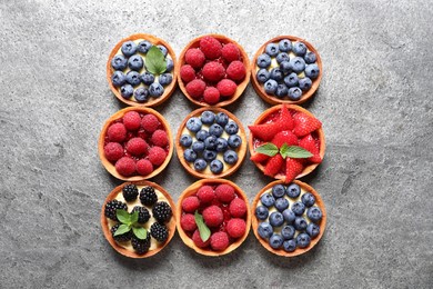 Tartlets with different fresh berries on light grey table, flat lay. Delicious dessert