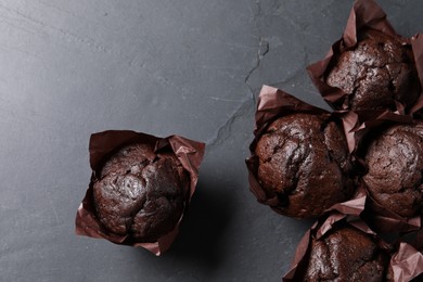Photo of Tasty chocolate muffins on black textured table, flat lay. Space for text