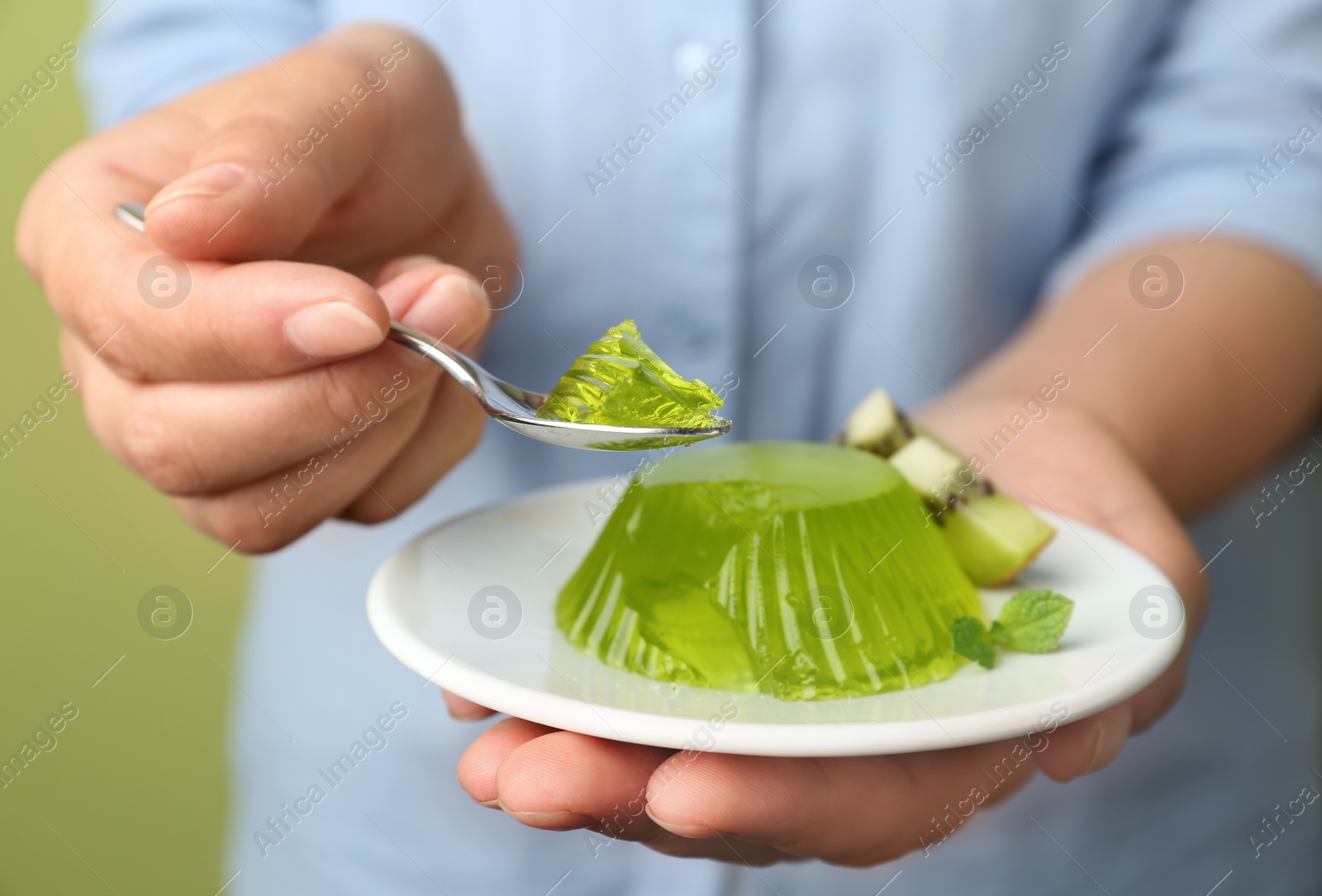 Photo of Young woman eating tasty kiwi jelly on green background, closeup