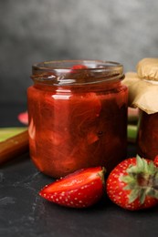 Photo of Jar of tasty rhubarb jam and strawberries on dark textured table