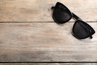 Stylish sunglasses on wooden background, top view. Space for text