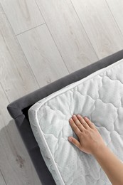 Photo of Woman touching soft light green mattress on bed, top view