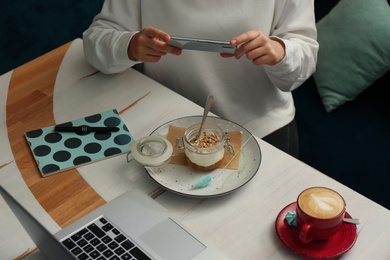 Blogger taking picture of dessert at table in cafe, closeup