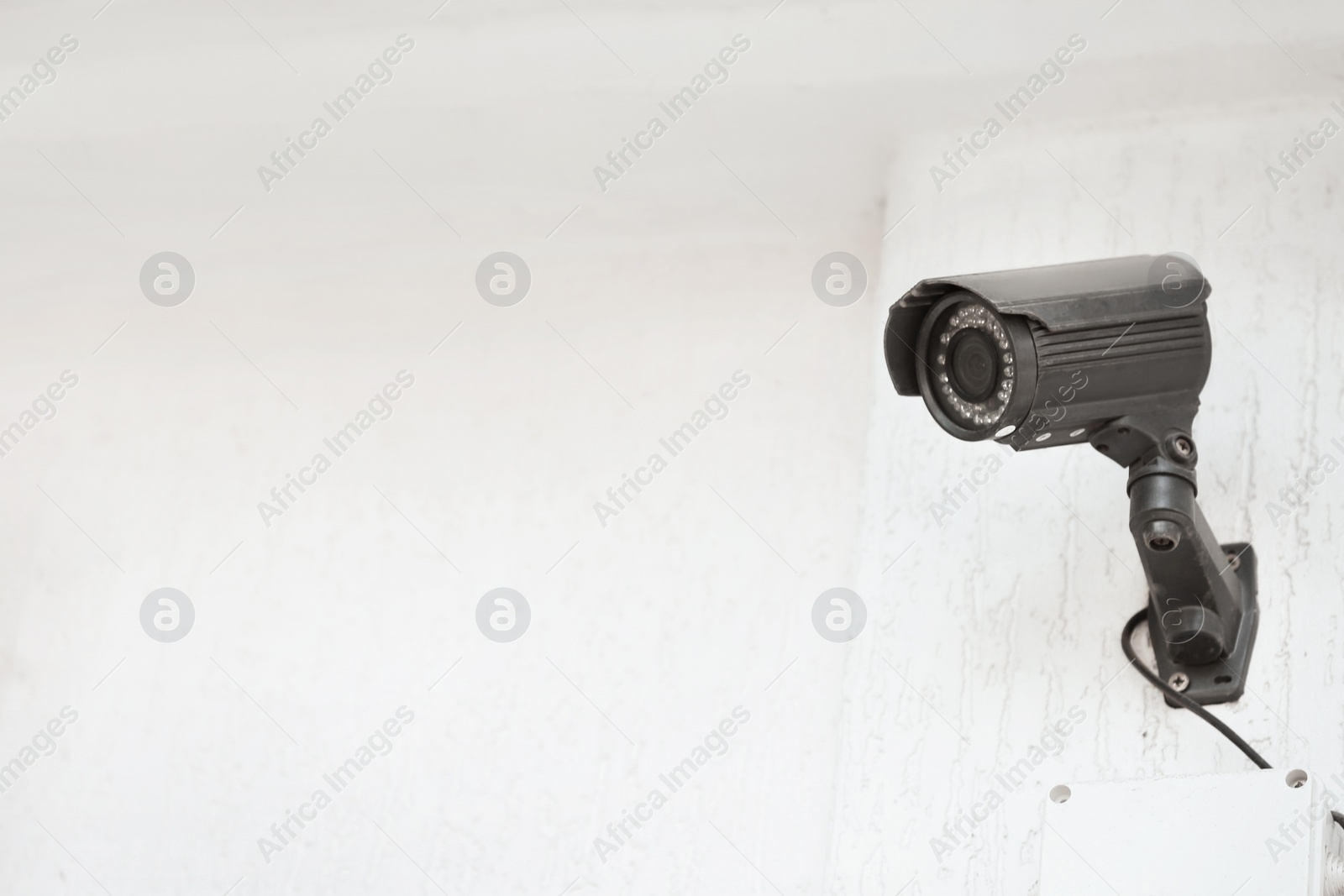 Photo of Modern CCTV security camera on white building wall outdoors. Space for text