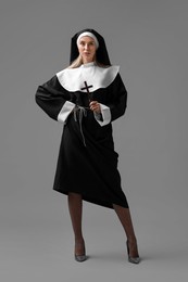 Photo of Woman in nun habit and mesh tights holding wooden cross on grey background. Sexy costume