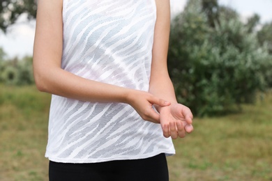 Photo of Young woman checking pulse after training in park, closeup