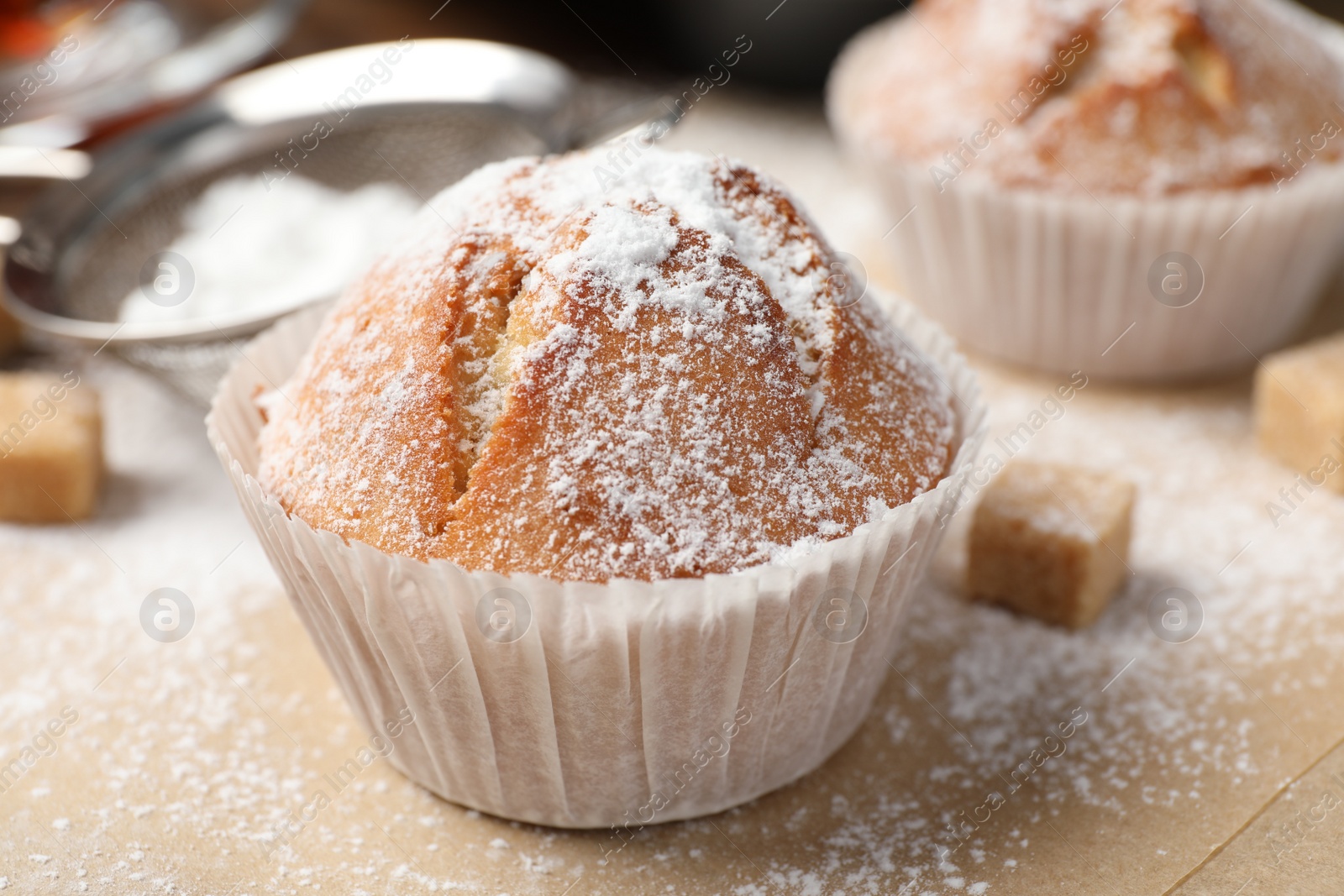 Photo of Tasty muffin powdered with sugar on table, closeup