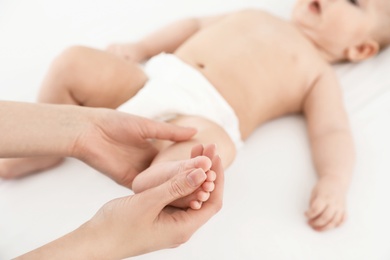 Photo of Mother and her cute child on white bed, closeup. Baby massage and exercises