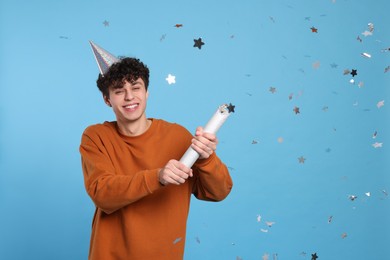 Photo of Handsome young man blowing up party popper on light blue background