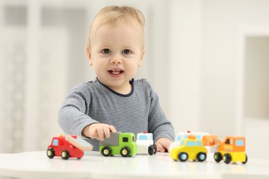 Children toys. Cute little boy playing with toy cars at white table in room