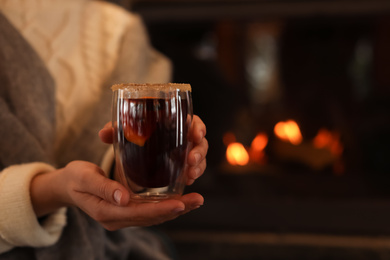 Photo of Woman with mulled wine near fireplace indoors, closeup. Winter vacation
