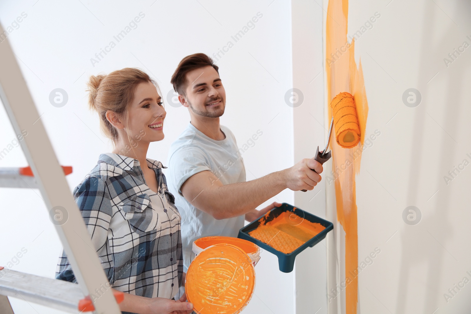 Photo of Happy couple painting wall indoors. Home repair