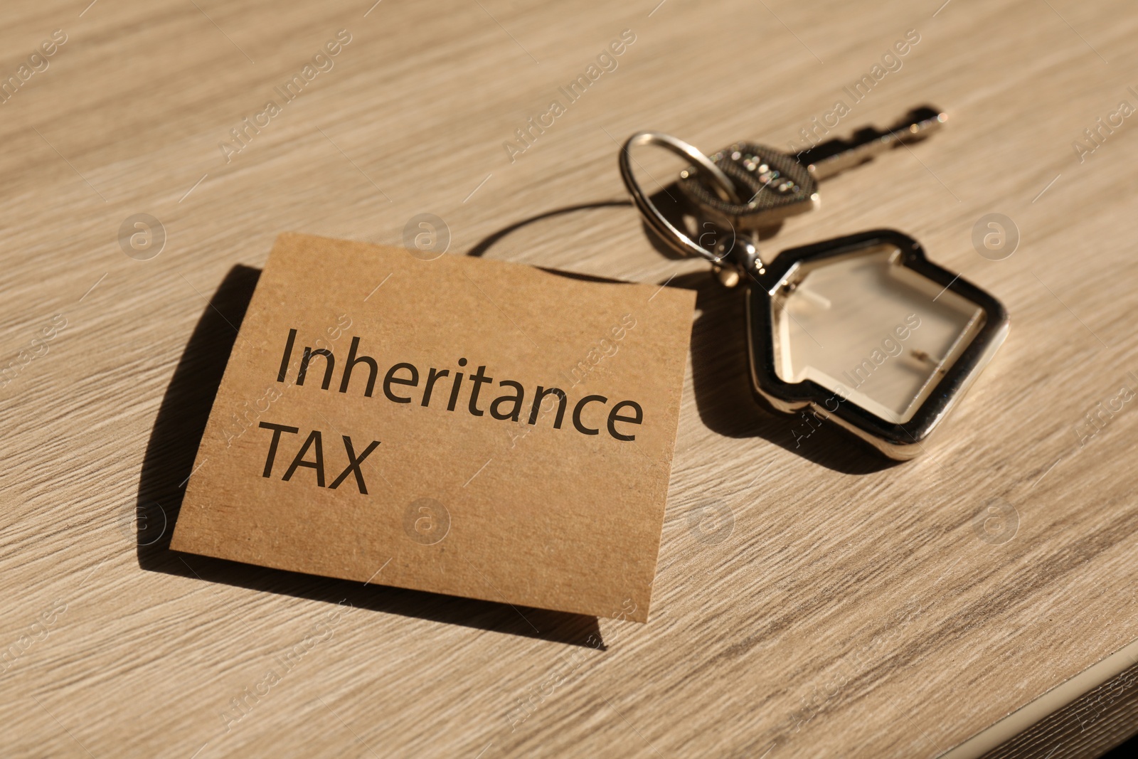 Photo of Inheritance Tax. Card and key with key chain in shape of house on wooden table, closeup