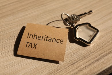 Photo of Inheritance Tax. Card and key with key chain in shape of house on wooden table, closeup