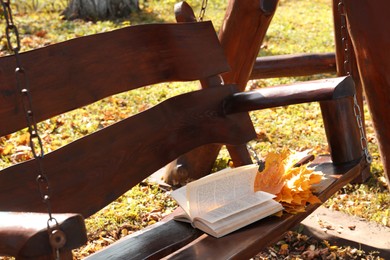 Wooden swing with book and yellow dry leaves outdoors. Autumn atmosphere