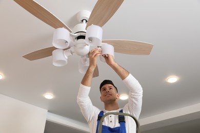 Photo of Electrician changing light bulb in ceiling fan indoors