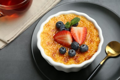Photo of Delicious creme brulee with berries and mint in bowl on grey table, closeup