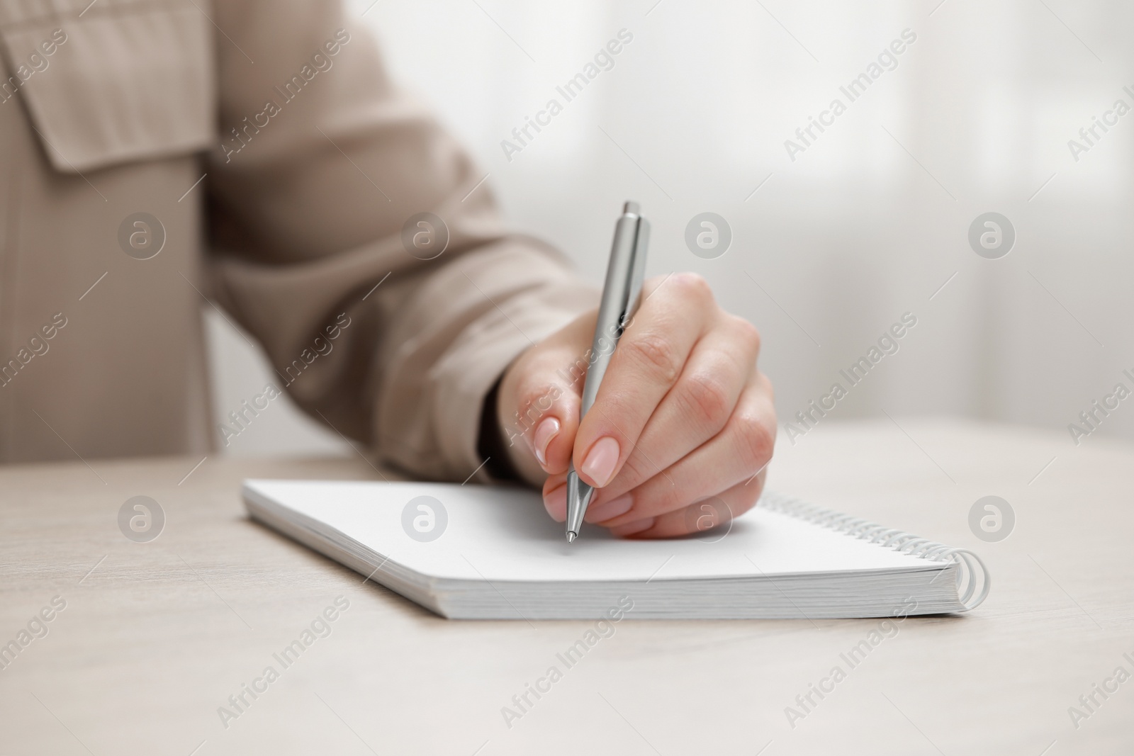 Photo of Woman writing in notebook at wooden table, closeup