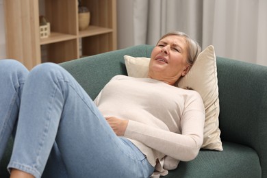 Photo of Menopause. Woman suffering from abdominal pain on sofa at home