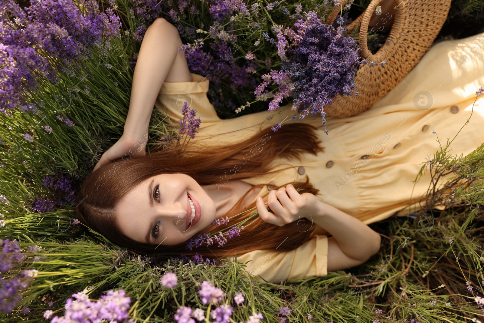 Photo of Young woman lying in lavender field on summer day, top view