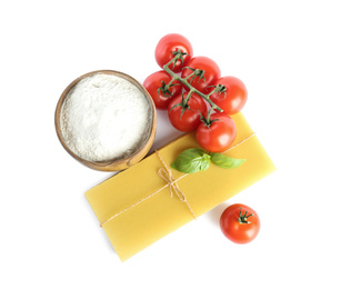 Uncooked lasagna sheets, tomatoes, basil and bowl of 
flour on white background, top view