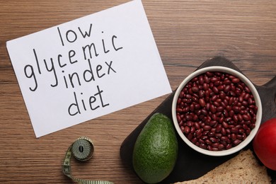 Photo of Paper with words Low Glycemic Index Diet, measuring tape and healthy products on wooden table, flat lay