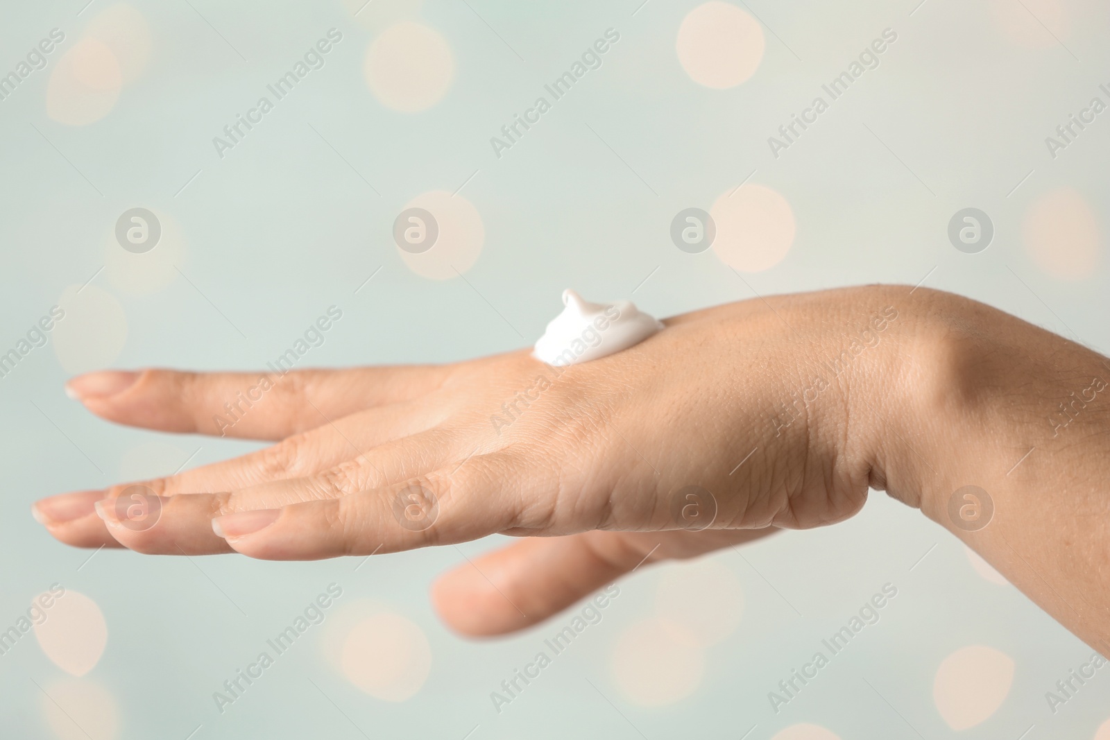 Photo of Woman applying hand cream on blurred background, closeup