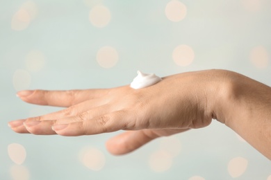 Photo of Woman applying hand cream on blurred background, closeup