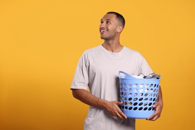 Photo of Happy man with basket full of laundry on orange background. Space for text