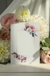 Photo of Blank invitation card, eucalyptus leaves and flowers on white wooden table
